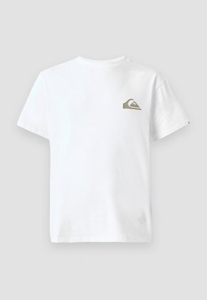 Jeune homme debout face à l'avant, portant un t-shirt blanc avec un petit logo sur la poitrine et un pantalon noir, avec un tatouage sur son avant-bras gauche.