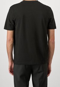 Černé bavlněné tričko s kulatým výstřihem, krátkými rukávy a rovný lem, doplněné tmavými, ušitými kalhotami. Jednoduchý design bez viditelných log.