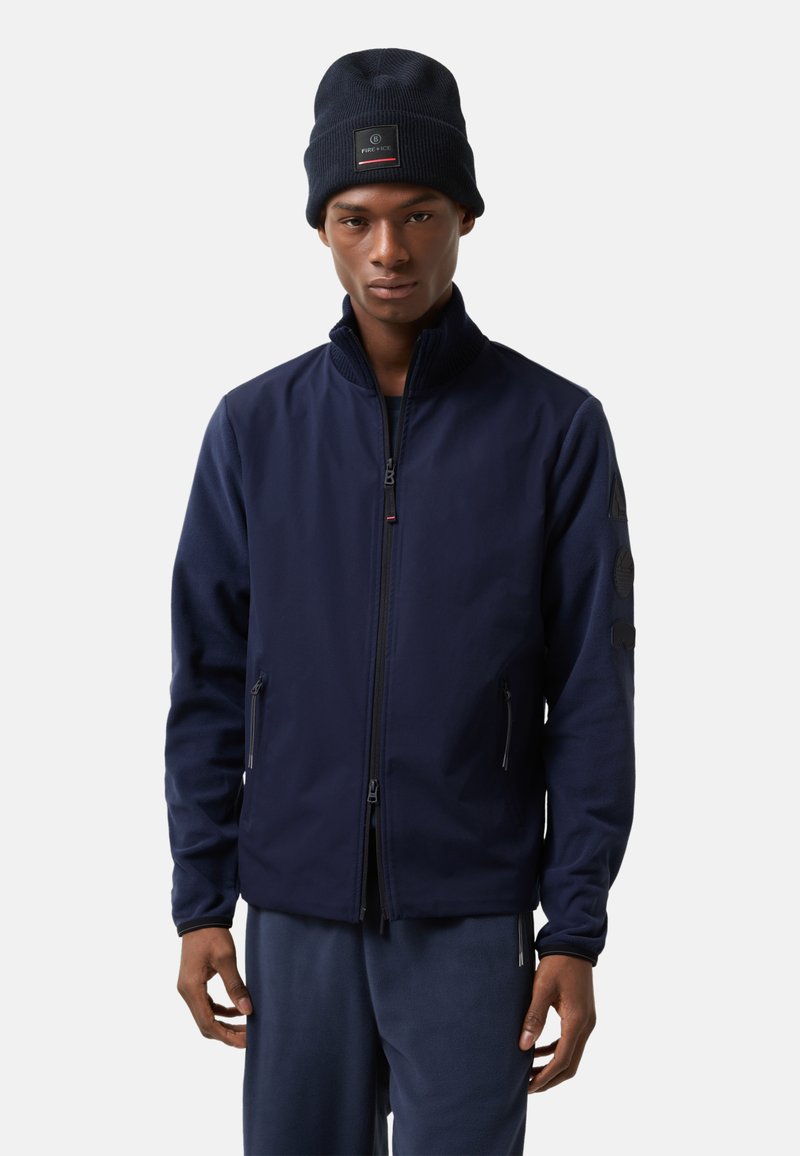 Marine fleece jack met ritssluiting aan de voorkant, hoge kraag en schuin geplaatste zijzakken. Draagt een bijpassende marine gebreide muts met een logo patch.