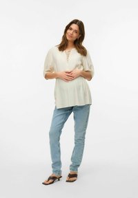 Lys beige bluse med puffede ærmer og en frontbånddetalje, parret med lyseblå lige ben jeans og sorte hæle-sandaler.