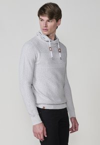 Lichtgrijze hoodie met textuurgebreide stof, voorzien van een hoge kraag, koorden met bruine accenten en een ribgebreide zoom.