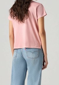 T-shirt en coton rose à manches courtes et coupe décontractée, associé à un jean taille haute bleu clair avec une étiquette logo sur la poche arrière.