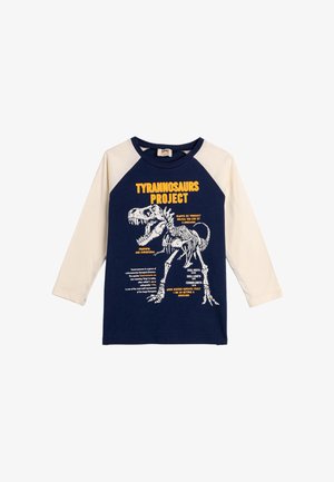 Langarm-T-Shirt mit einem marineblauen Körper und cremefarbenen Ärmeln. Grafik eines T. rex-Skeletts mit Text in Gelb und Weiß. Aus Baumwollmaterial.