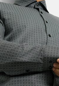 Schwarz-weiße gemusterte Hemd mit geometrischem Design, Button-Down-Kragen, auffälligen schwarzen Knöpfen und einer glatten Textur.