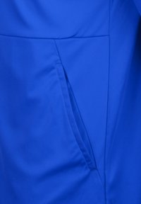 Blauer Stoff mit glatter Textur, seitlicher Taschenkonstruktion und strukturierten Nähten für ein maßgeschneidertes Erscheinungsbild.