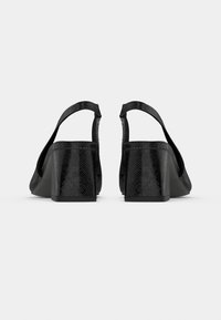 Μαύρα πέδιλα με λουράκι στο πίσω μέρος με υφή, χοντρό τακούνι και φαρδιά λουράκια. Λεπτομέρειες με λείο φινίρισμα στα λουράκια και κομψή σιλουέτα.