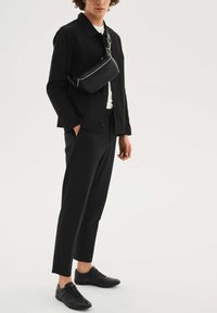 Čierny ležérny outfit pozostávajúci z sako na gombíky, zužovaných nohavíc a crossbody tašky, všetko z hladkej látky s minimalistickým dizajnom.