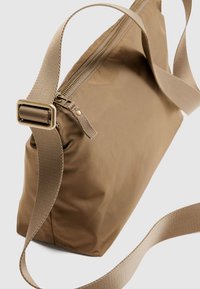 Καφέ ώμου τσάντα από νάιλον με φερμουάρ, λεία υφή και φαρδιά ρυθμιζόμενη λουρίδα. Διαθέτει χρυσούς μεταλλικούς ρουχισμούς.