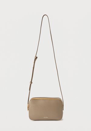 Geantă mică taupe de tip crossbody cu fermoar auriu și curea reglabilă, logo Calvin Klein pe partea din față, pe un fundal alb simplu.