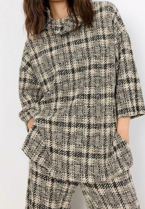 Top de punto a cuadros beige y negro con cuello vuelto, mangas anchas y grandes bolsillos delanteros. Combinado con pantalones a cuadros a juego.