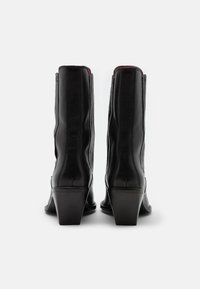 Stivali ankle in pelle nera con tacco affusolato, caratterizzati da dettagli di cuciture verticali e una finitura liscia. La vista posteriore mostra una vestibilità aderente.