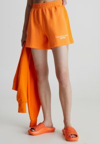 Oransseista puuvillasekoitteisista shortseista, joissa on joustava vyötärö ja "Calvin Klein Jeans New York" -logo. Yhdistetty vastaavan värisiin oransseihin liukuasusti ja huppariin.