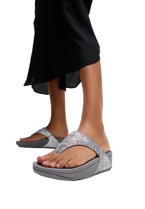 Voeten met grijze platformsandalen met glinsterende bandjes, gecombineerd met een zwarte rok van middelbare lengte.