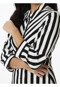 Mustavalkoinen raidallinen nappikauluspaita, jossa on kaulus ja käännetyt hihat. Paita on valmistettu sileästä kankaasta ja siinä on kontrastinen viivakuvio.