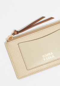 Portafoglio in pelle beige con finitura testurizzata, dotato di una tasca frontale liscia, chiusura a zip e un cinturino in pelle marrone.