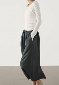 Haut blanc à manches longues associé à un pantalon large gris foncé, ample et à poches latérales, en tissu texturé. Design minimaliste.