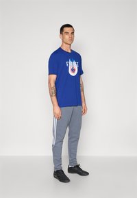 Zila kokvilnas T-kreklu ar grafiku "FRANCE" logo, apvienots ar pelēkām sporta biksēm ar baltām svītrām un melniem sporta apaviem.