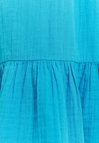 Turkoosi kangas, jossa on teksturoitu pinta, kerrostettu paneeli, tasainen sävygradientti ja kevyet rypyt.