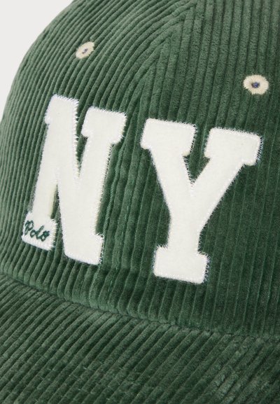 Căciulă verde din catifea rib câtuie cu litere brodate albe "NY", detalii de cusătură subtile și un mic orificiu de accent pe vârf.
