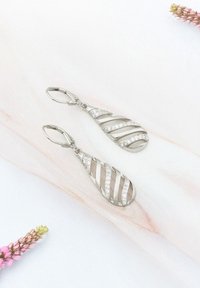 Silverhängande örhängen med en tårform, som har diagonala utskärningar och glittrande stenar längs ena sidan. Slätt, polerat yta.