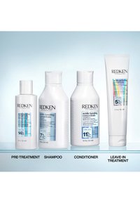Cuatro botellas de cuidado capilar Redken etiquetadas como pre-tratamiento, champú, acondicionador y tratamiento sin enjuague con fórmulas concentradas de unión ácida.