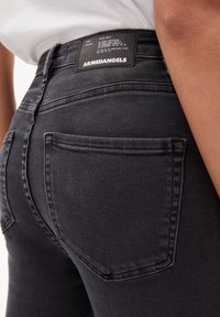 Černé džíny z denimu s hladkým povrchem, standardními zadními kapsami a štítkem s pokyny k údržbě na pasu.