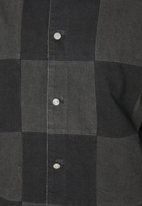 Kariertes Hemd aus schwarzem und grauem Stoff mit weicher Textur, ausgestattet mit Metallknöpfen und klassischem Kragen.