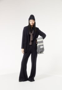 Marineblauer Nadelstreifenanzug mit weitem Bein, kombiniert mit einer braunen Krawatte und einem grau gestreiften Schal. Eine schwarze Mütze und Schuhe runden den Look ab.