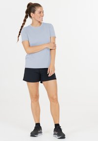 Ljusblå kortärmad skjorta kombinerad med svarta sportshorts och mörka löparskor. Skjortan har en rund halsringning och en slät textur.