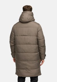 Hustá, polstrovaná, kabát do kolien v tlmenej olivovej farbe. Má vysokú kapucňu a horizontálne švy s zacvakávacími uzáverkami na leme.