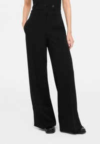 Pantaloni neri a gamba larga in tessuto morbido, con una vestibilità dritta e tasche laterali. Presentano una vita strutturata e una piega sottile sul davanti.