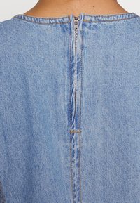 Ljust blå denimplagg med dragkedja på baksidan, synliga sömmar och en slät struktur. Enkelt design med minimal detaljering.