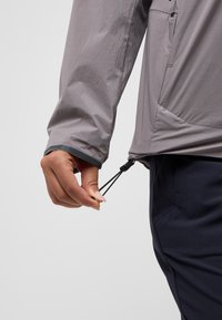 Gray lightweight jacket with elastic cuffs, adjustable hem, and a zipper pocket. The fabric features a fine texture, emphasizing functionality.