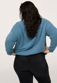 Maglione blu fuzzy con design corto e vestibilità ampia, abbinato a jeans in denim scuro. Il maglione ha una finitura strutturata e spalle scese.