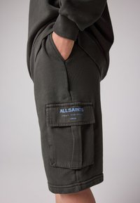 Mörkgröna cargoshorts i mjukt tyg, med sidoficka med blå branding och ribbad midjeresår.