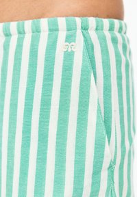 Mintgrön och vitrandig tygshorts med dragsko i midjan, med en liten logodetalj. Texturen verkar mjuk och lätt.