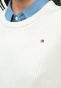 Λευκό πλεκτό πουλόβερ με υφασμένο μοτίβο και ριμπ λαιμόκοψη, με μικρό κόκκινο, λευκό και μπλε λογότυπο στο στήθος.