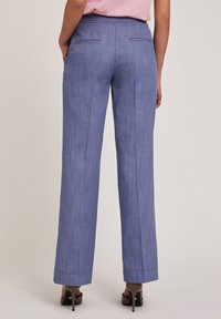 Lichtblauwe, wijde broek met een subtiele textuur, voorzien van twee achterzakken en gestikte details op de zoom. Gemaakt in combinatie met hoge hakken.