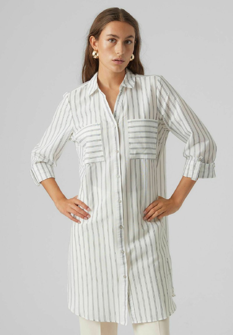 Camicia bianca con bottoni, con righe verticali nere, dotata di due tasche sul petto e maniche arrotolate, realizzata in tessuto leggero.