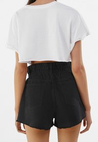 Bílé crop tričko s pohrnutými rukávy spojené s černými džínovými šortkami s vysokým pasem, elastickým pasem a třepeným lemem.