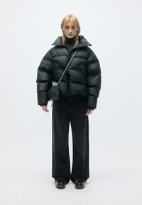Sort cropped puffer jakke med rektangulære bælgfag, parret med brede mørke jeans og klodsede sorte sko. Crossbody taske med kæderekke.