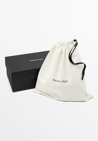 Cotton drawstring bag in cream with "Massimo Dutti" print, alongside a sleek black rectangular box featuring the same brand name.