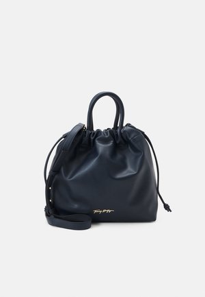 Bolso de mano de cuero negro con cordón, doble asa, correa de hombro desmontable y un sutil logo dorado en el centro frontal.