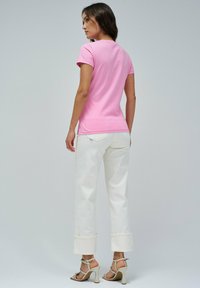 Camiseta rosa de manga corta combinada con pantalones de pierna ancha blancos con dobladillos enrollados y tacones de tiras beige. Se observa una textura de tela suave.