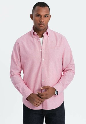 Helles rosa Hemd mit Knopfleiste und Tasche, strukturierter Stoff, Umlegekragen und langen Ärmeln, kombiniert mit dunklen Jeans.