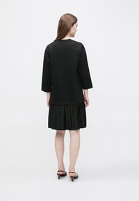 Czarna sukienka z dopasowaną górą i plisowaną spódnicą, wykonana z gładkiego materiału. Posiada rękawy do połowy ramienia oraz długość do połowy łydki.