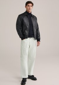Chaqueta bomber de cuero negra con cuello alto, combinada con pantalones rectos de color verde claro. Tejido texturizado y calzado contrastante.