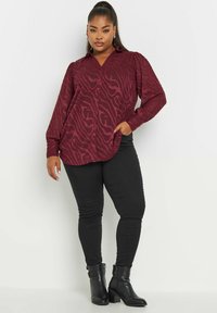 Blusa borgogna con un motivo a strisce zebrate, maniche lunghe e chiusura con bottoni. Abbinata a pantaloni skinny neri e stivaletti.
