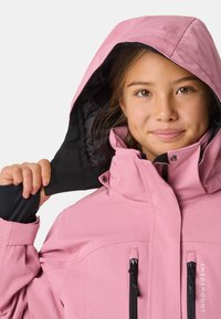 Veste imperméable rose avec une capuche noire, un col montant et des poches zippées. Conçue en tissu durable et avec des poignets ajustables.