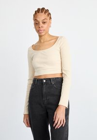 Top corto a maniche lunghe beige a coste con scollatura ampia e design aderente, abbinato a jeans neri a vita alta.